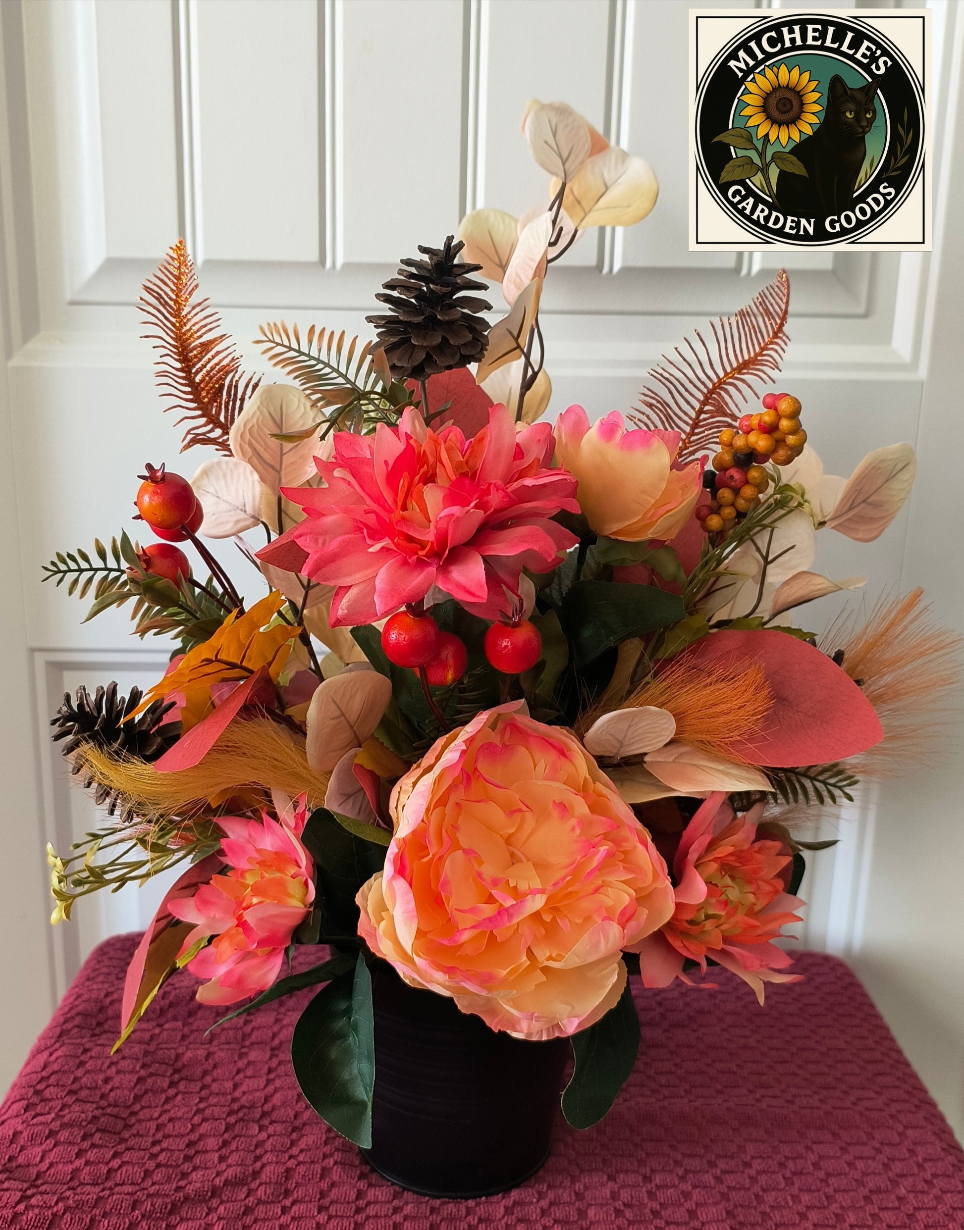 Floral arrangement with pink and orange flowers on a pink surface, featuring Michelles Garden Goods logo.