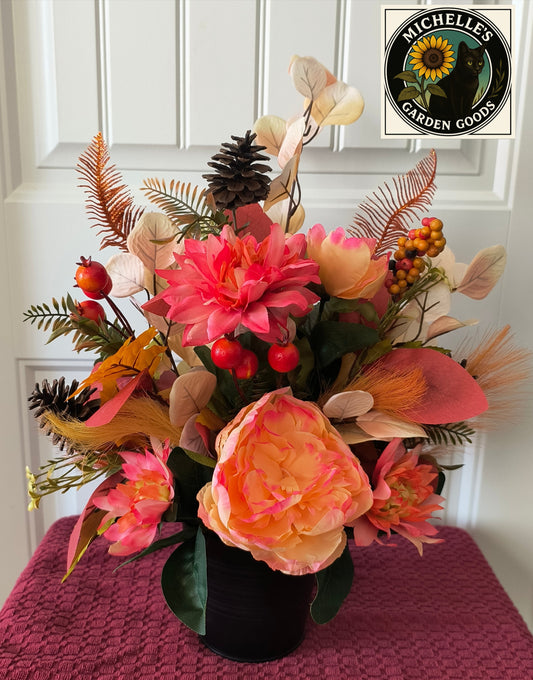 Floral arrangement with pink and orange flowers on a pink surface, featuring Michelles Garden Goods logo.